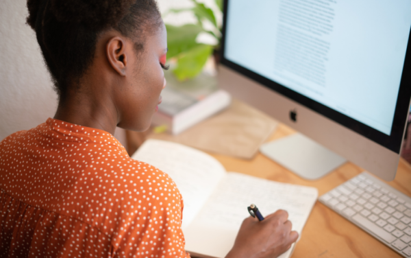 author writing in a notebook in front of a computer